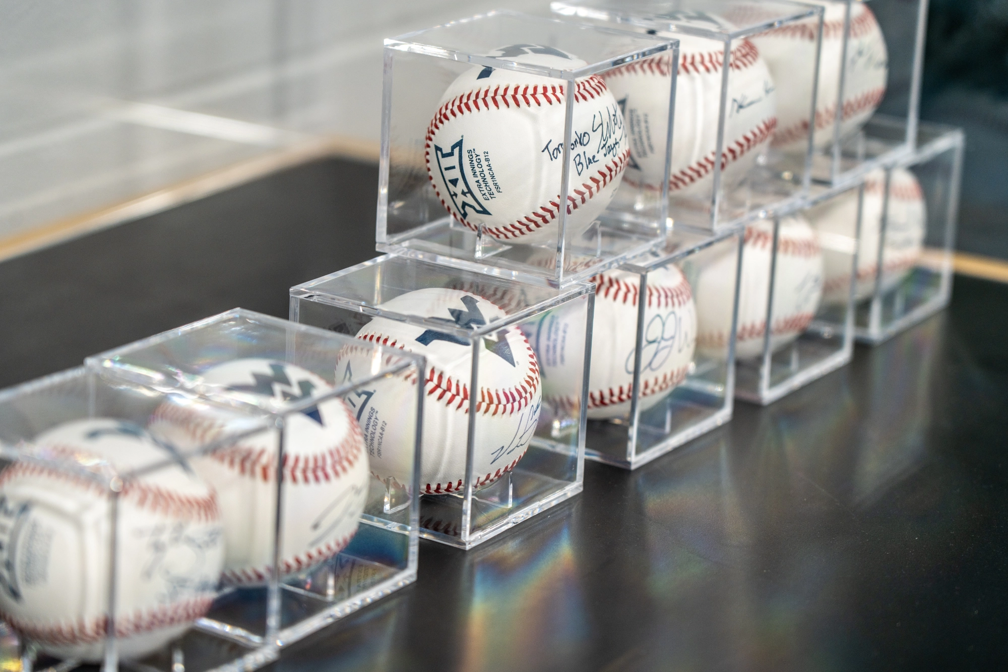 Autographed baseballs displayed in clear acrylic cases arranged in rows on a table.