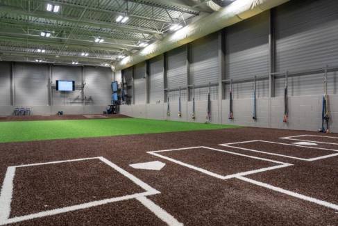 An indoor baseball training facility with turf flooring, batting areas, and wall-mounted resistance equipment.