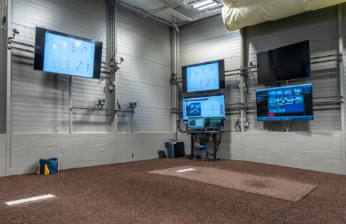 An indoor baseball training lab with multiple wall-mounted screens displaying data and video analysis.