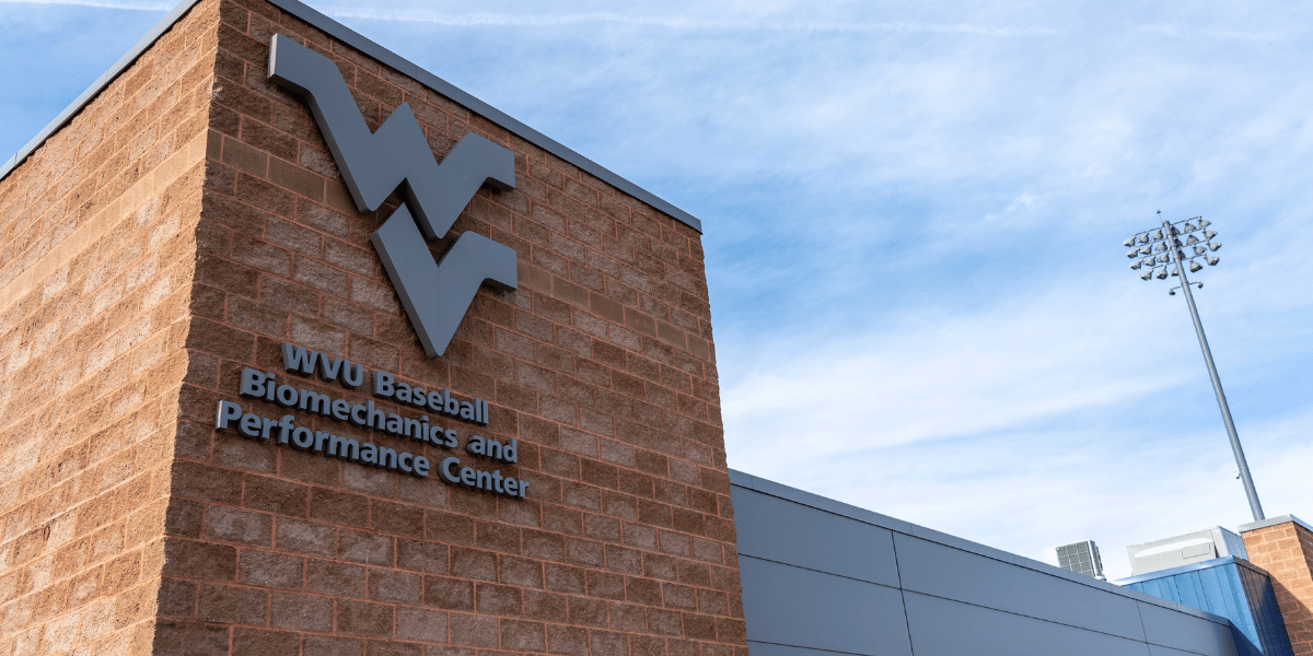 Exterior of a building corner with a large WV logo and the text “WVU Baseball Biomechanics and Performance Center.”
