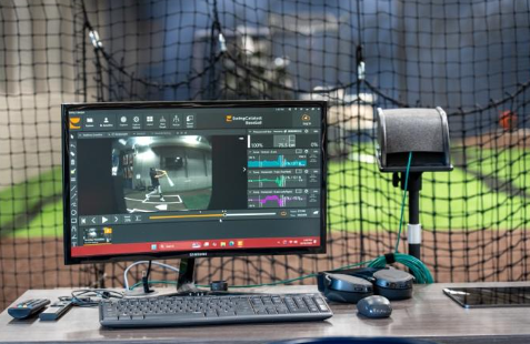 A computer monitor displays baseball swing analysis software inside an indoor training facility.